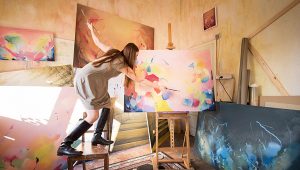 mulher correndo risco fazendo o que ama. Pintando uma grande tela em cima de uma cadeira.