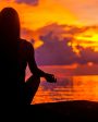 mulher meditando em frente ao mar no pôr do sol